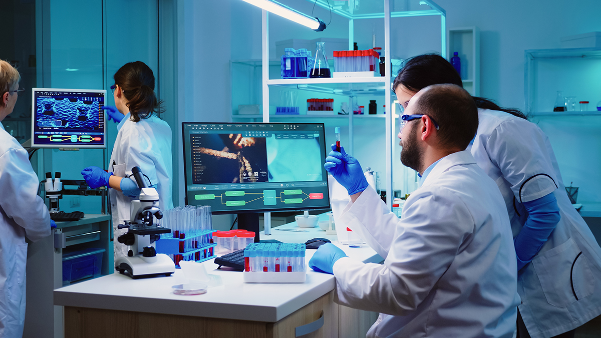 Doctor taking a blood sample tube from rack with machines of analysis in the lab background